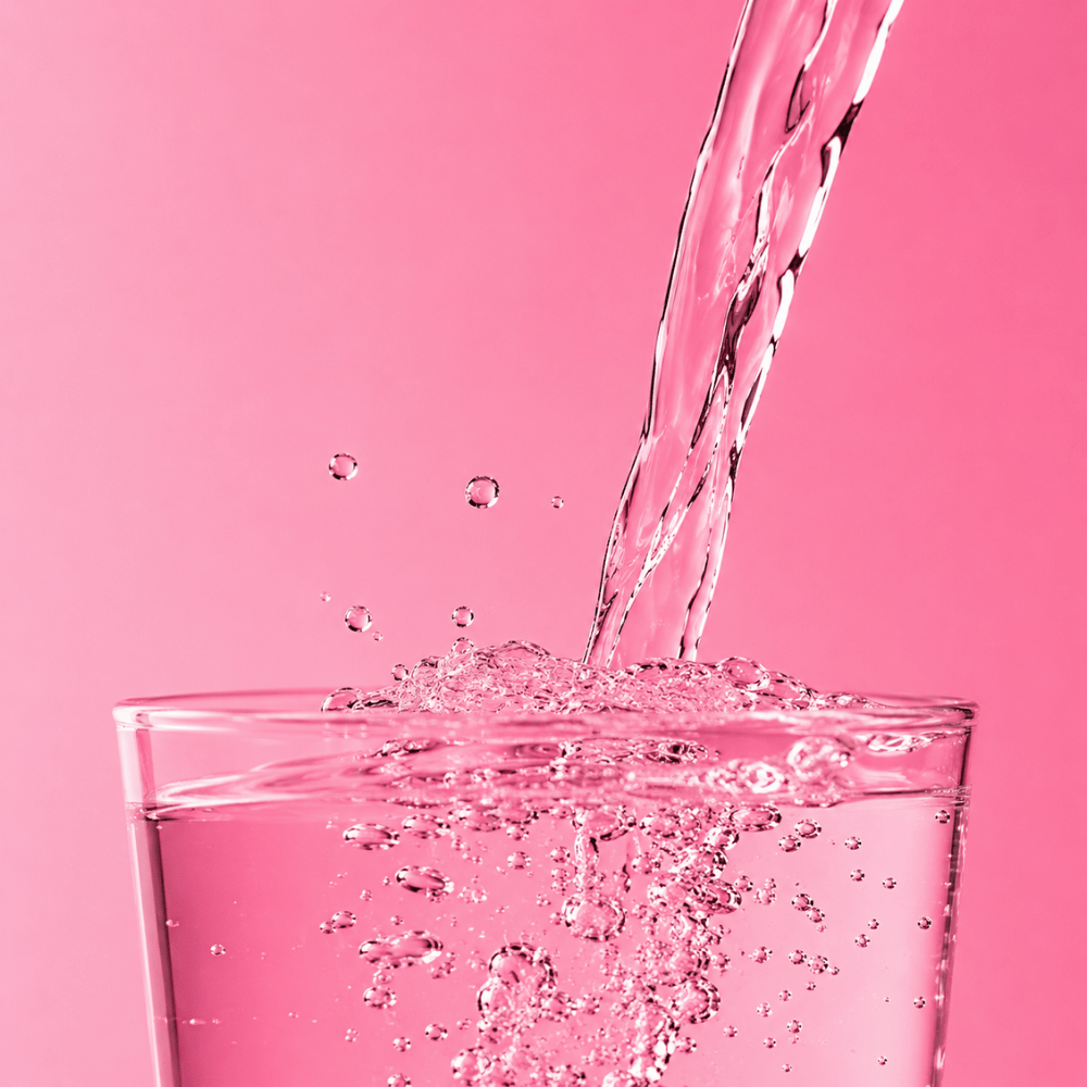 Eau gazeuse qui coule dans un verre sur fond rose